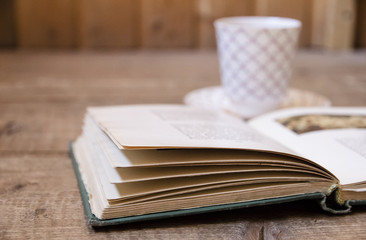 Opened old book and blurred glass of tea in background on  wooden surface