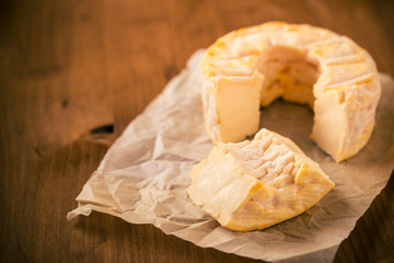 Portion cut from whole golden camembert cheese on wooden table