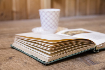 Opened old book and blurred glass of tea in background on  wooden surface