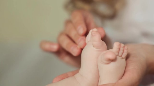 Mother's hands gently touch the little feet of her baby