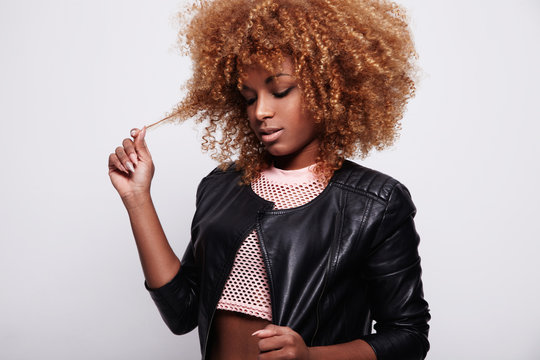 black woman toches her curly blonde hair wears leather jacket