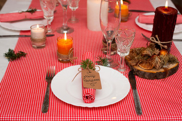 Festive composition with candles and plates. Table decoration. A beautiful table setting, red table cloth, tablecloth in the box. Christmas dinner. A Napkin decorated with inscription Merry Christmas.