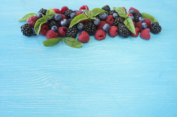 Various fresh summer berries on wooden background. Ripe raspberries blackberries blueberries and basil leaves. Berries at border of image with copy space for text.
