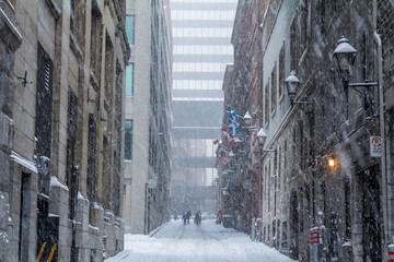 Street of Old-Montreal in winter under a snow storm with a modern skyscraper in the background