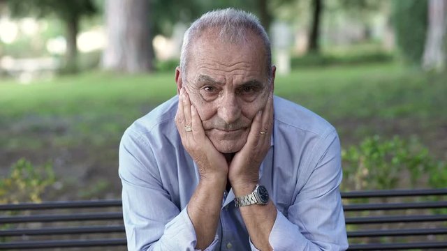  sad retiree on a park bench looking at the camera sadly