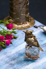 Steampunk bronze bird on glass cup on blue wooden tray.