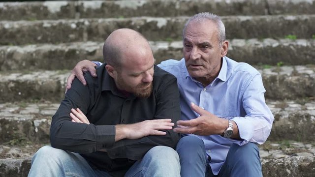 father and son on a bench in a park, talking and comparing