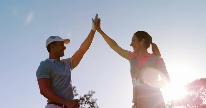 Two happy golfers giving high five at golf course 