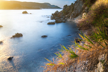 Long exposure seascape at sunrise. View of the cliff into the sea and distant islands. In the backlight sunbeam light. Paleokastrica. Corfu. Ionian archipelago. Greece.