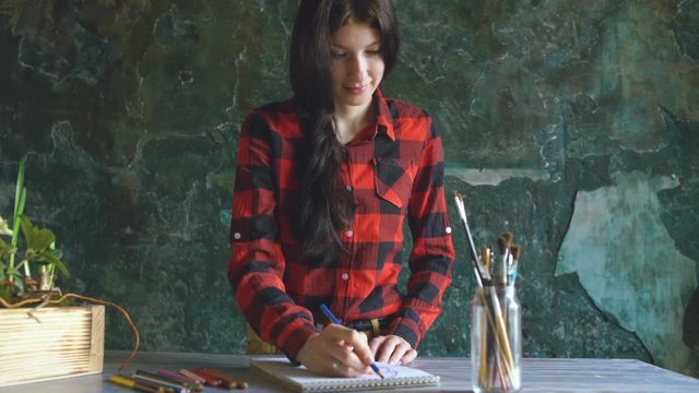 Young woman artist painting scetch on paper notebook with pencil and smile