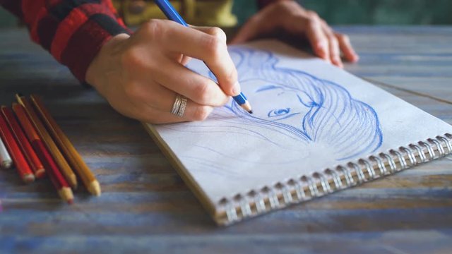 Young woman artist painting scetch on paper notebook with pencil closeup
