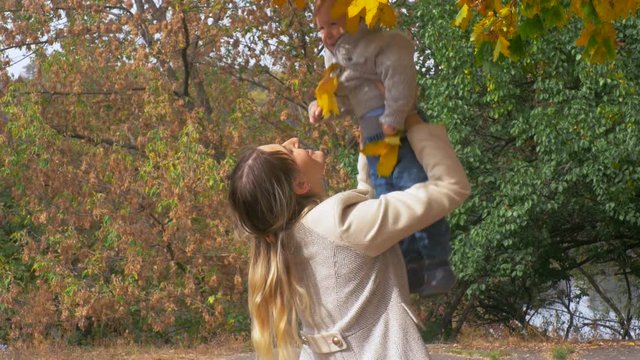 4K closeup footage of happy young mother hugging and throwing here baby son at autumn park