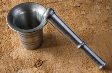 Metal mortar and pestle on rough wooden background texture.