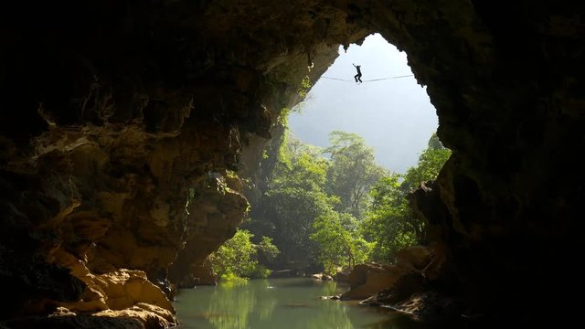 Tightrope walker in mountain cave with tropical forest on background