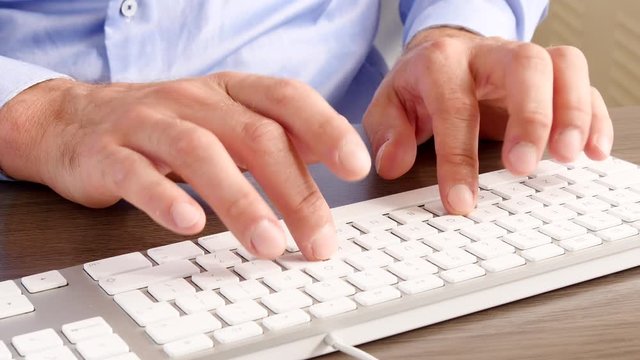 Close up businessman typing a keyboard at a desk with blue shirt
