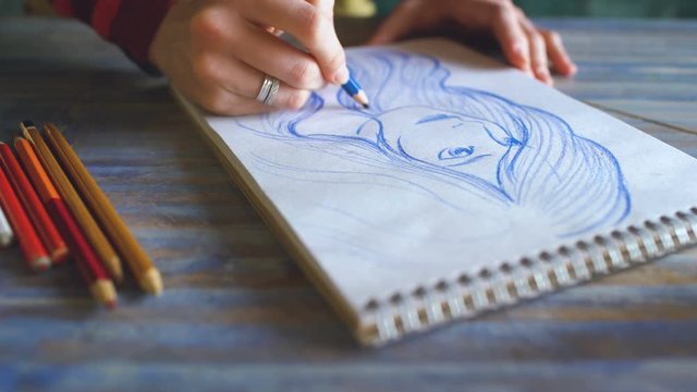 Young woman artist painting scetch on paper notebook with pencil closeup
