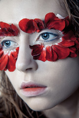 beauty portrait of young fashion model with wet hairs and red flower petals around her eyes. studio shot on blue background.