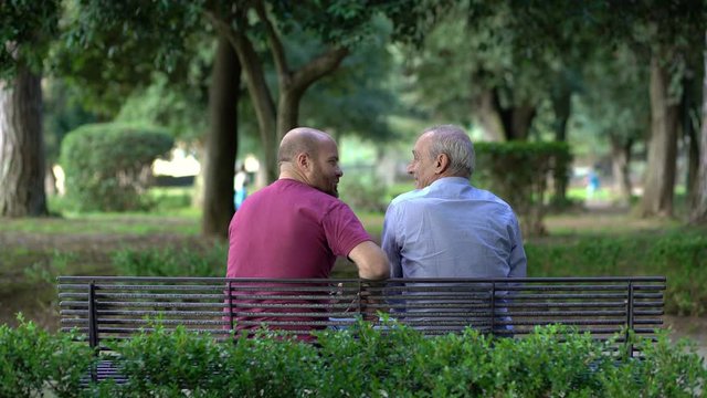 father and son on a bench in a park, talking and comparing