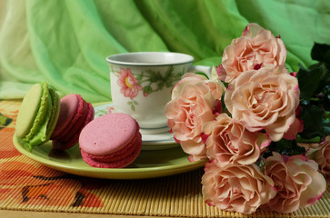 Pink roses, cup of tea, cake macaroon on a background of green silk.