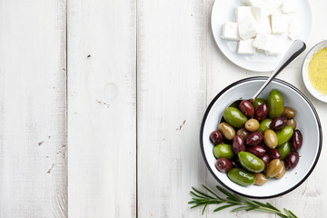 Fresh olives mix, feta cheese, rosemary twigs and olive oil on white wooden background