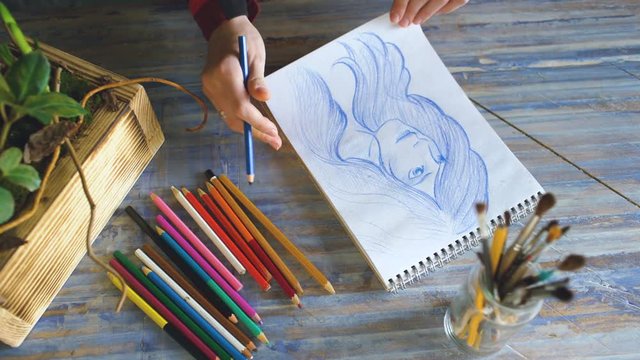 Young woman artist painting scetch on paper notebook with pencil closeup