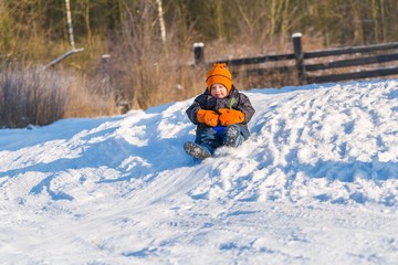 Fototapeta na wymiar Happy little caucasian boy downhill on plastic slider or sledge