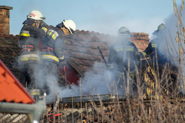 Fototapeta premium Firefighters fighting with house fire on the roof