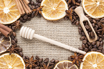 orange slices, cinnamon, star anise and coffee beanc with wooden scoop and honey dipper on canvas background. Image with copy space