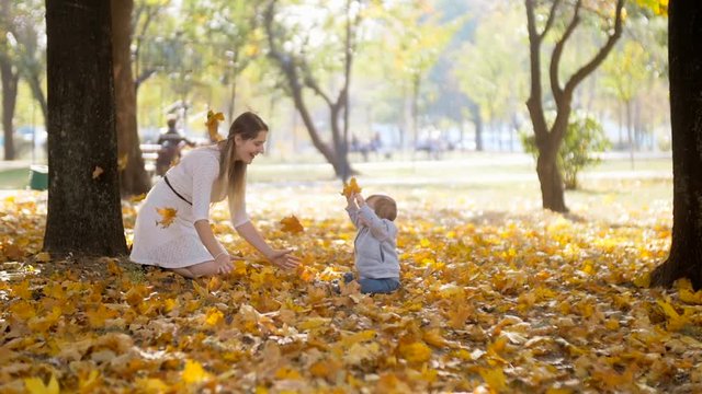 Slow motion footage of happy young mother and her baby son playing with fallen leaves at autumn park