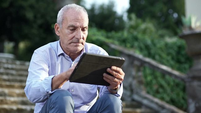 old man sitting on the steps use the tablet