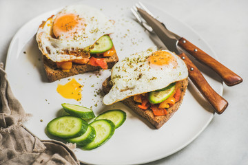 Breakfast toasts with vegetables and fried egg on white plate over grey marble background, selective focus, horizontal composition. Healthy, clean eating, dieting food concept
