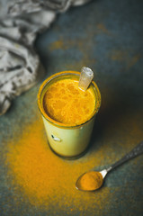 Golden milk with turmeric powder in glass over dark background, copy space. Health and energy boosting, flu remedy, natural cold fighting drink. Clean eating, detox, weight loss concept