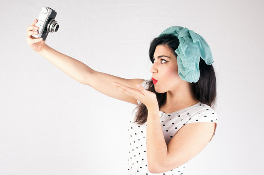 pinup style girl with red lips on a white background is holding an old reflex camera