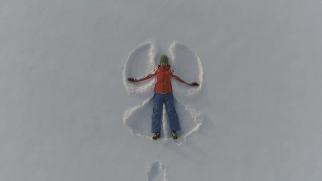 Woman making snow angels and playing in snow. Aeriel view from the drone