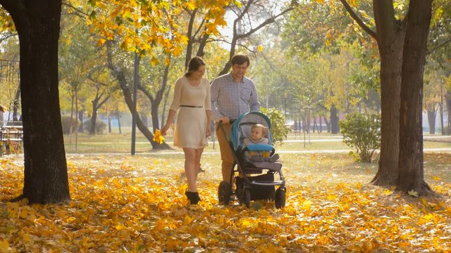 4K footage of happy young parents walking with baby in pram at autumn park