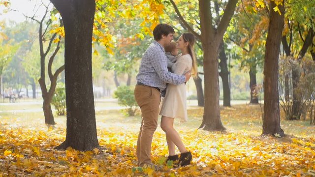 Slow motion footage of happy young parents holding their baby son and kissing at autumn park