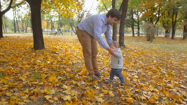 Slow motion footage of young carin father teaching his baby son first steps at autumn park
