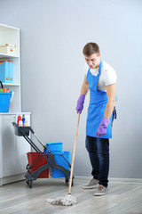 Young man with mop cleaning floor at office
