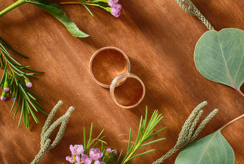Closeup of wedding rings and flowers on wooden background