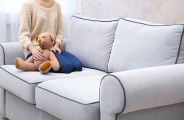 Young girl sitting with fluffy teddy bear on sofa in room