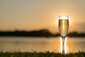 A glass of Champagne on grass at river side In the evening background