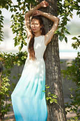 Young sensual woman in long white and blue dress outdoors poses. Professional style.