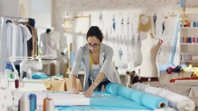 Beautiful Female Fashion Designer Draws on a Piece of Fabrics. She Works in a Light Colorful Studio Full of Various Clothes, Fabrics and Sketches. Shot on RED EPIC 4K (UHD).