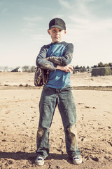 Boy with arms crossed wearing a  baseball glove and holding the