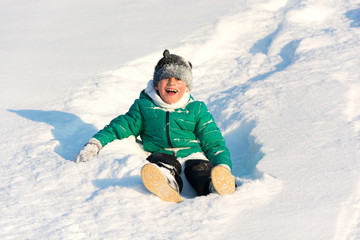 Fototapeta na wymiar Boy playing in the snow. Sledding on a snowy hill. Winter games. Baby joy of snow. Throwing snowballs.