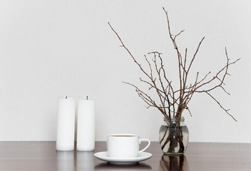 Cup, candles and branches in bottle on a wooden table. Romantic grey and white still life