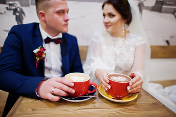 Newlyweds sitting on table at cafe with two cups of coffee