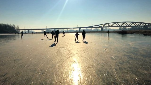Ice skating people on a frozen lake near the river IJssel in The Netherlands during a beautiful winter day