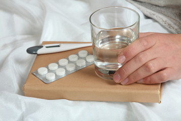 Close-up of man's hand holding a glass of water next to the pills, thermometer. Disease.