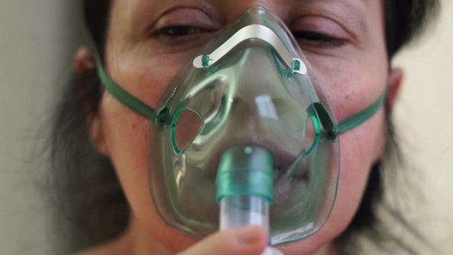 Close up shot of a woman wearing a medical nebulizer breathing mask that administers medicines to help alleviate persons with lung problems.